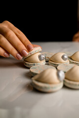Female confectioner's hand covers a macaroon with the other half decorated with a decorative edible pearl