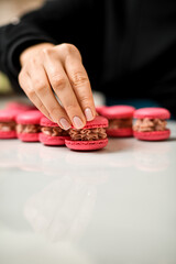 Side view of red macaroons each covered with beige cream in a curvy shape