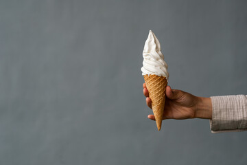 Ice cream in a waffle cone close-up, held by a woman's hand on a gray background.