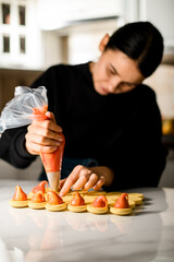 Cute female confectioner squeezes pink cream from a pastry bag onto beige macaroons