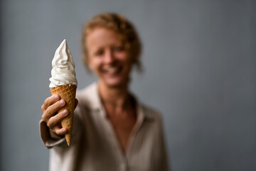 A girl with blond curly hair, of European appearance, holds ice cream in a waffle cone in her hand...