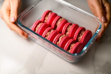 Close up of glass rectangular container with red macaroons held by female hands of pastry chef