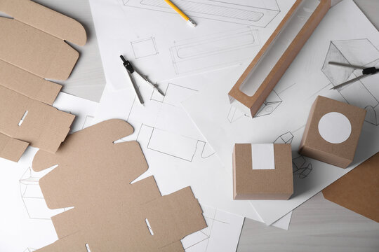 Creating packaging design. Drawings, boxes and stationery on light wooden table, flat lay