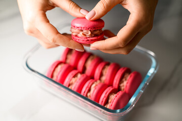 Focus on red macaroon in female hands holding it directly above other red macaroons
