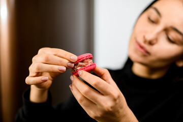 Focus on red macaroon in female hands, which pastry chef holds in front of her