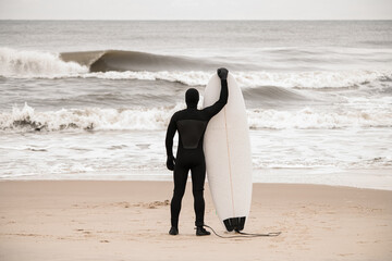 Slender male surfer stands on the seashore and holds his surfboard - 790777344