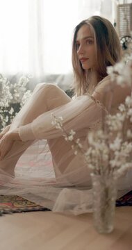 Young elegant model wearing vintage bridal dress sitting on floor, posing at home in stylish vintage interior