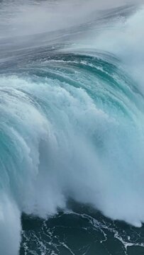 Slow motion aerial shot of powerful wave crashing. Sea or ocean big stormy surf clear turquoise water with foamy white texture. Vertical Screen