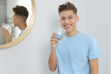 Young man with mouthwash in bathroom. Oral hygiene