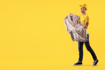 Dry-cleaning delivery. Happy courier holding coat in plastic bag on orange background, space for...