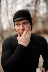 Young male surfer wearing a wetsuit rubs water repellent cream on his face