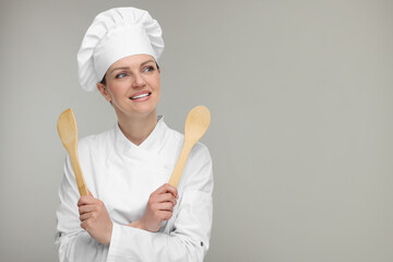 Naklejka premium Happy woman chef in uniform holding wooden spoon and spatula on grey background, space for text