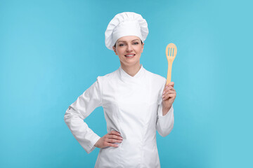 Happy chef in uniform holding wooden spatula on light blue background