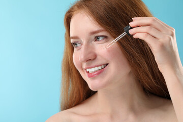 Smiling woman with freckles applying cosmetic serum onto her face against light blue background, closeup. Space for text