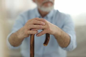 Grandpa with wooden walking cane indoors, closeup