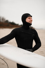 Smiling male surfer walking on the sandy seashore with a white surfboard in his hands