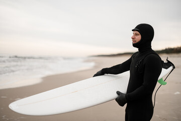 Smiling male surfer standing on the sandy seashore with a white surfboard in his hands - 790783761