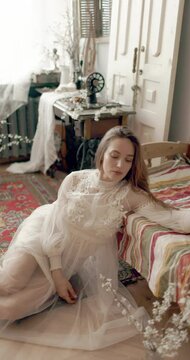 Young elegant model wearing vintage bridal dress sitting on floor, posing at home in stylish vintage interior