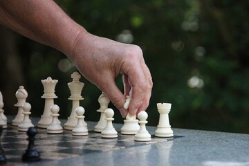 Close-up of a hand about to move the knight in chess outside in the garden on a stone chess table