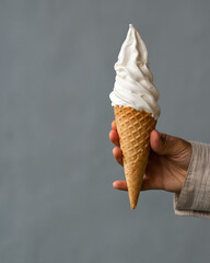 Ice cream in a waffle cone close-up, held by a woman's hand on a gray background.