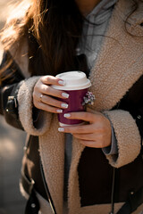 Female hands with wedding ring on a finger hold a disposable cup with coffee