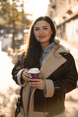 Young pretty smiling woman is holding a disposable cup with coffee