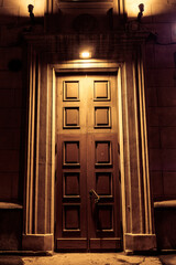 A dark wooden door with a light shining on it. The door is open and the light is coming from the top