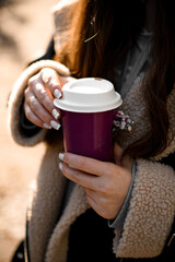 Female hands hold a disposable cup of coffee with a small bouquet of flowers