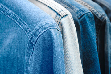 A row of denim jackets are hanging on a rack. The jackets are all different shades of blue and white