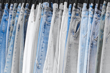 A row of jeans with different colors and patterns. The jeans are hanging on a rack