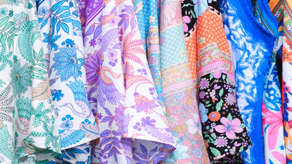 A row of colorful clothes with floral designs. The clothes are hanging on a rack. The colors are bright and cheerful, and the designs are intricate and detailed