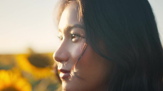 Closeup face of Asian woman opening eyes on sunset background. Young female looking straight at the sunflower field landscape