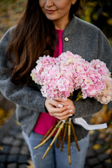 Focus on a bouquet of large-leaved hydrangeas in the hands of a young smiling woman