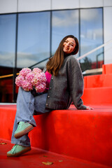 Young smiling pretty woman sitting with a bouquet of pink large-leaved hydrangeas on red steps