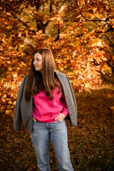 Cute smiling woman with long hair stands against a background of trees with crimson leaves