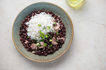 Rustic plate with cuban-style black beans and white rice, horizontal shot on a light-beige stone background, above view, copy space