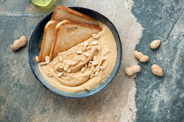 Bowl with peanut butter and toasted bread, horizontal shot on a beige and grey granite background, above view with space