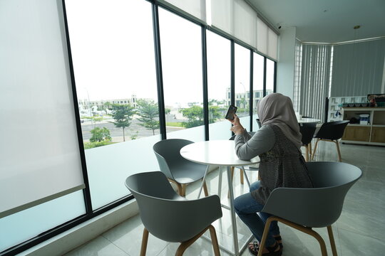 Portrait of woman sitting in cafe. Asian woman wearing hijab sitting alone in cafe holding cellphone to send message