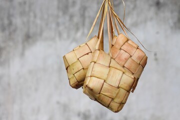 Ketupat (Rice Dumpling) on gray wall background. Ketupat is a natural rice casing made from young coconut leaves for cooking rice during eid Mubarak. Copy space for text card design.