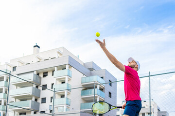 A man in a pink shirt is playing tennis with a yellow ball