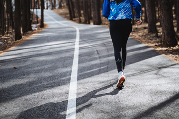 Athlete running on asphalt road through woods for outdoor exercise