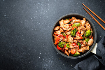 Chicken stir fry with vegetables and sesame at black background. Traditional asian cuisine.