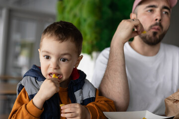 The little boy and his dad go together. Dad and son eating french fries. Dad and son time.
