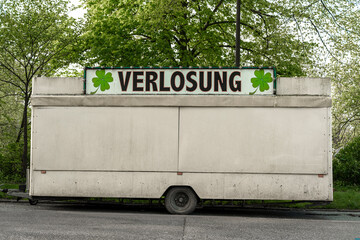 Ein geschlossener weißer Schaustellerwagen mit einem Schild auf dem VERLOSUNG steht, am...