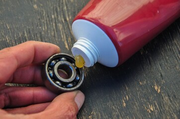 bearing in hand and a tube of lubricant on a dark wooden background. bearing lubrication