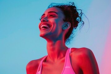 Young woman smiling and looking up at the camera in front of pink and blue background wearing a sports bra