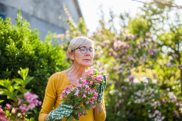 Happy senior woman enjoys in  the smell of flowers in her garden.