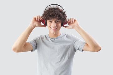 Smiling and handsome, the young man wears headphones and is isolated against a gray background. He looks at the camera with his blue eyes while listening to music