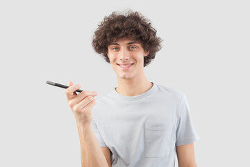 A young, handsome man smiles as he uses his smartphone, talking and listening with cellphone while looking into the camera with his blue eyes. He is isolated against a gray background