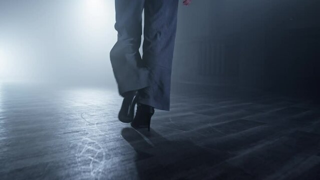 Young woman entering stage with smoke on background. Silhouette of dancer legs walking through dark studio. Woman legs on heels. Dancer's legs. Close-up shot in 4K, UHD
